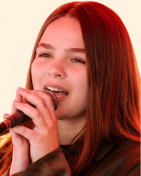 Porträt von Magdalena Lorenz: junge Frau mit langen roten Haaren, die in ein Mikrofon singt.